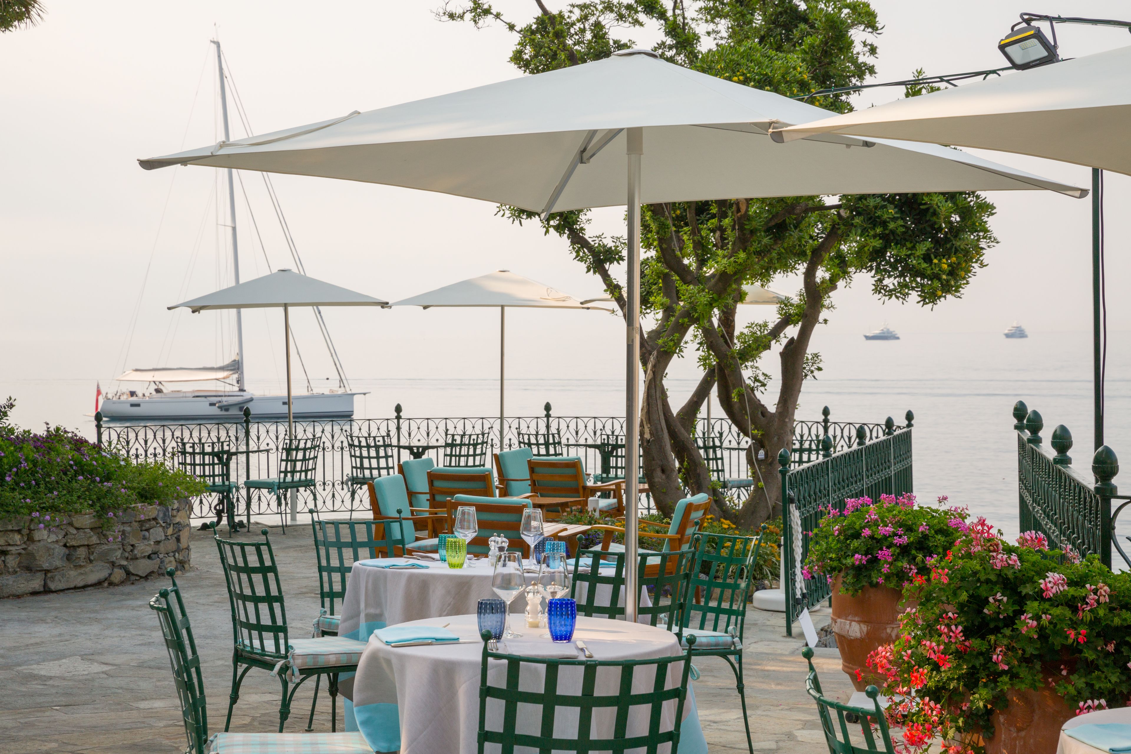 An outdoor dining area with tables and chairs, umbrellas, and a view of the sea.