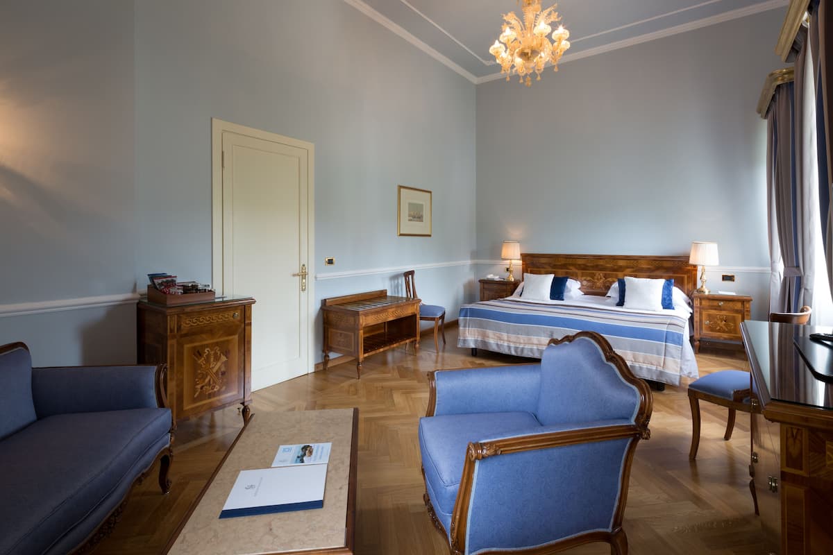 A hotel room with a bed, a sofa, a chair, a wooden cabinet, and a chandelier.