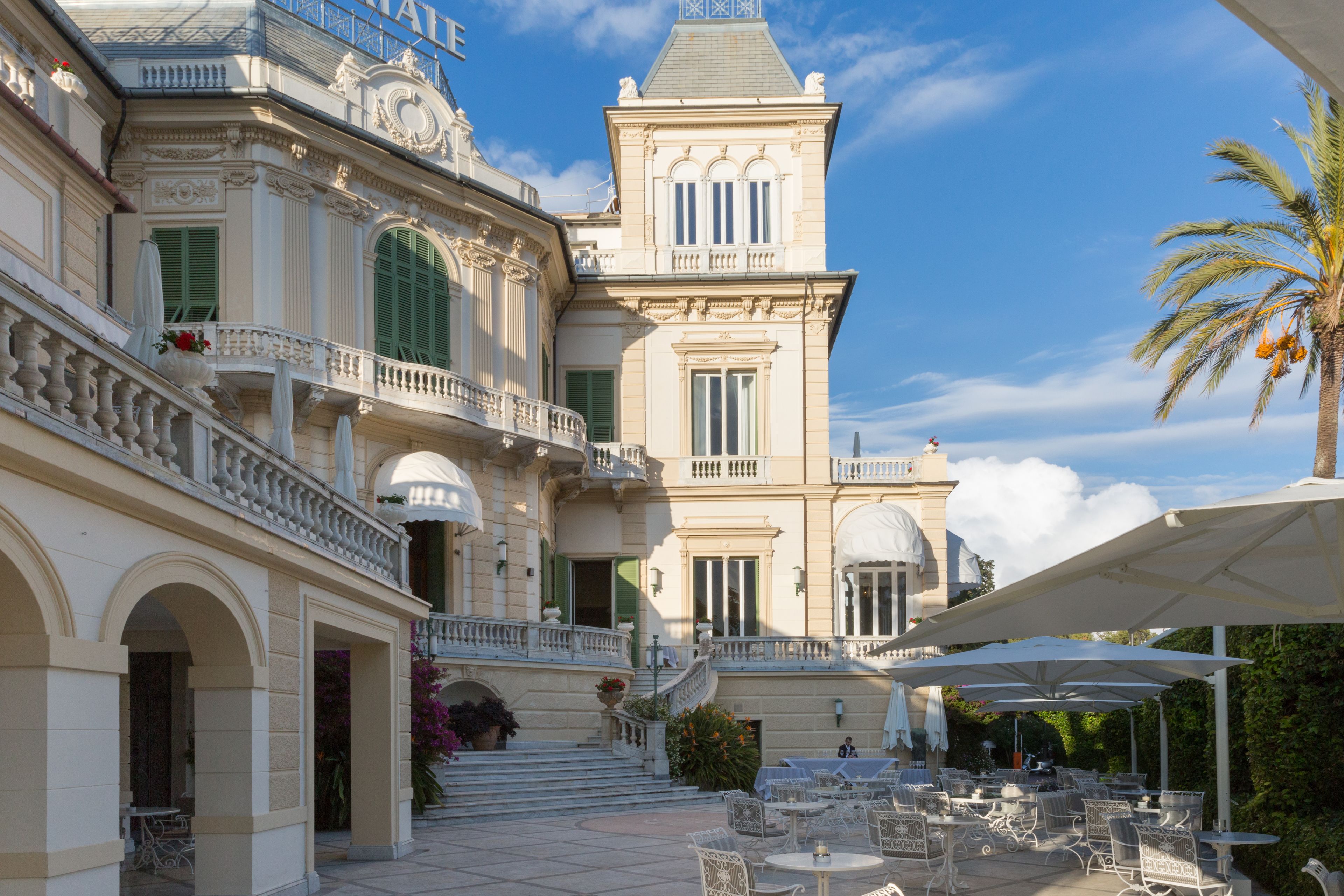 A grand building with a balcony, outdoor seating area, and a staircase leading to the entrance.