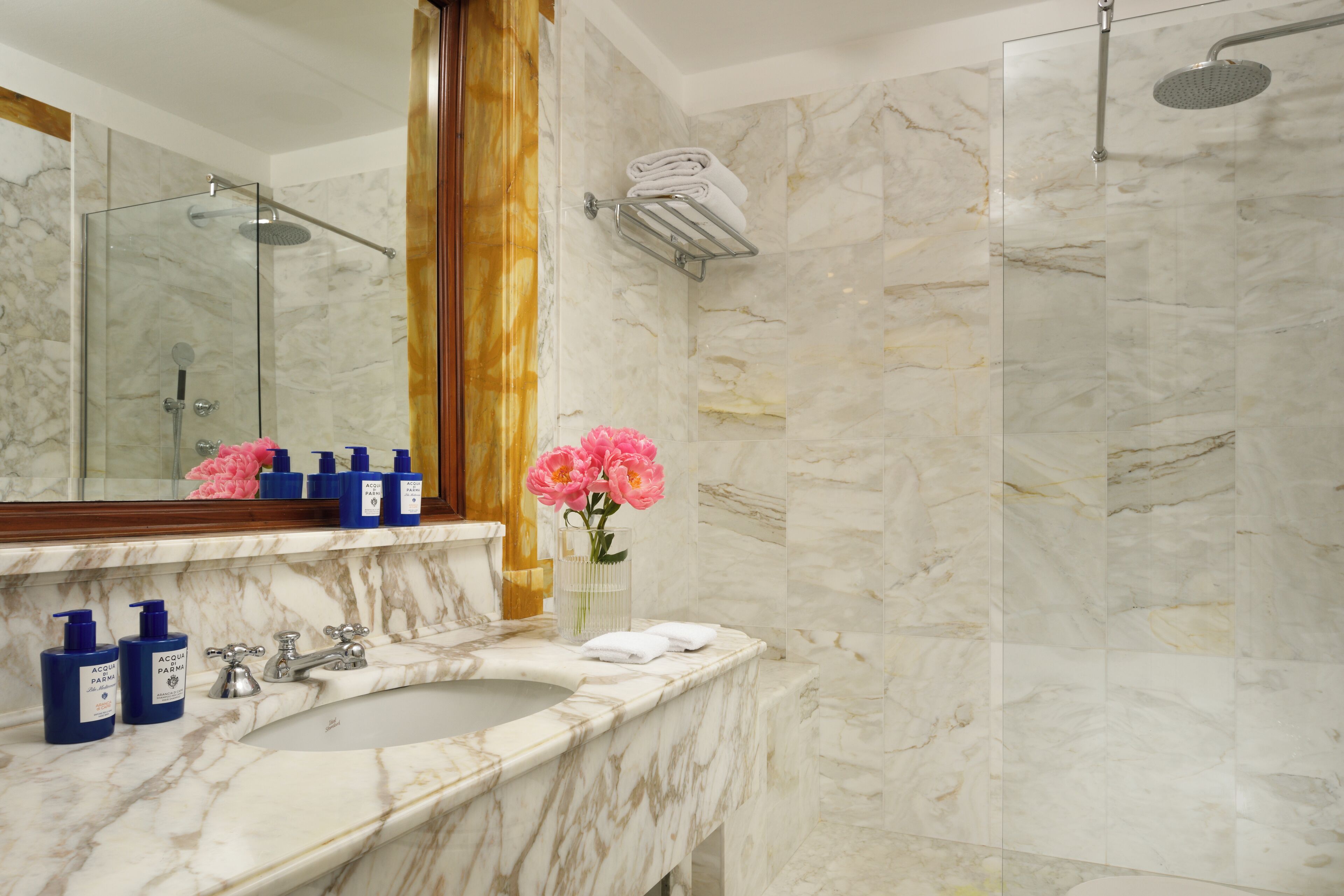 Une salle de bain avec un lavabo en marbre, une cabine de douche en verre et un miroir avec un cadre en bois.
