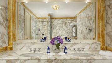 A marble bathroom with dual sinks, a large mirror, and a shower.