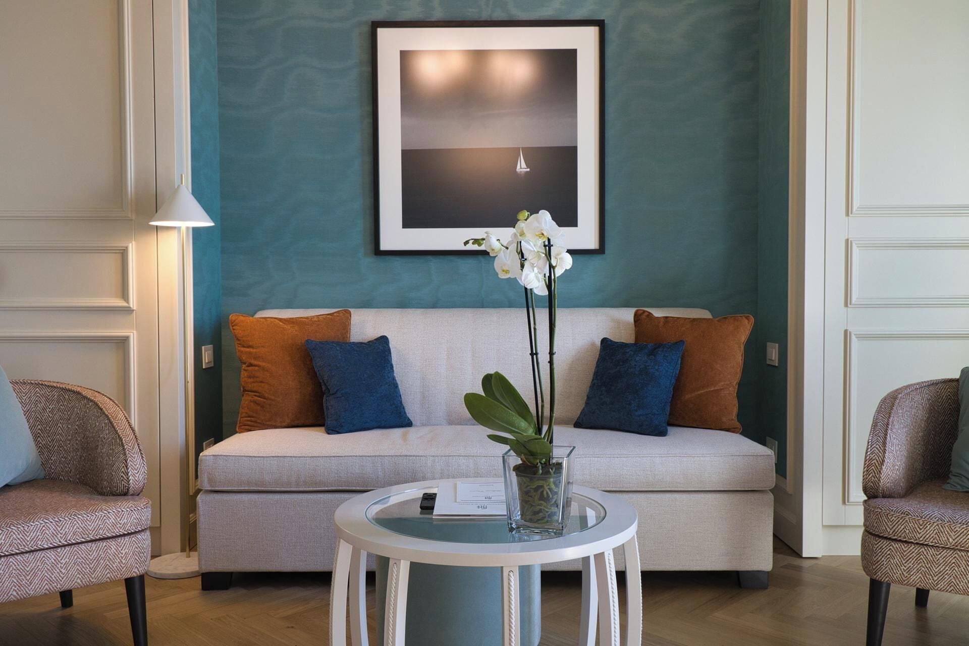 A living room with a sofa, two armchairs, a round table with a vase of flowers, and a framed picture on the wall.