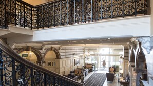 A grand lobby with a staircase, ornate railings, and a chandelier.