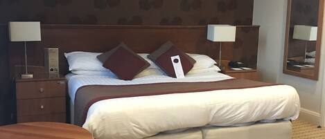 A hotel room with a large bed, two bedside tables with lamps, a round table, and a checkered floor.