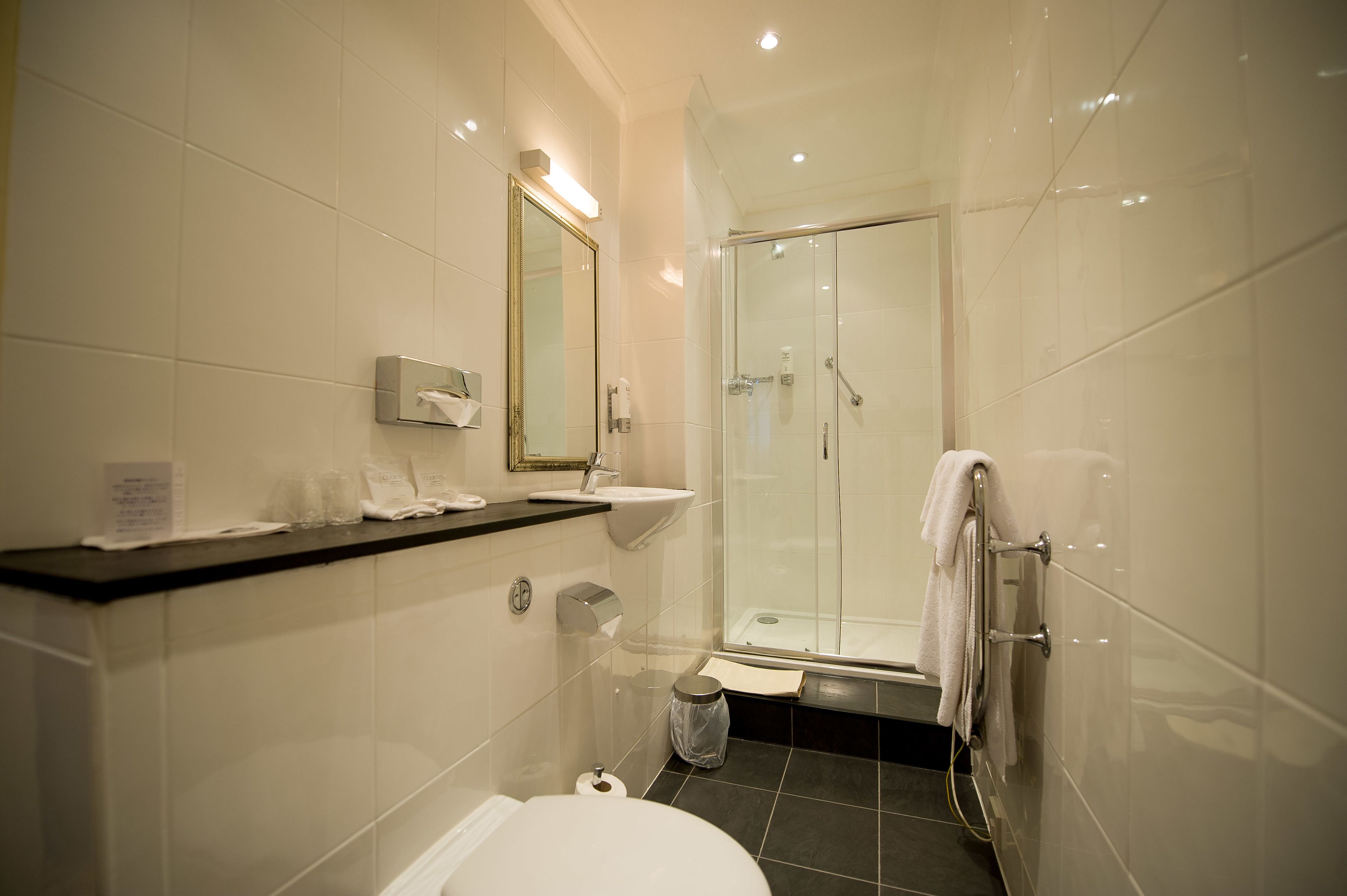 Un baño moderno con ducha de vidrio, azulejos blancos, lavamanos y retrete.