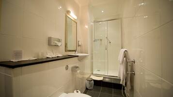 Un baño moderno con ducha de vidrio, azulejos blancos, lavamanos y retrete.