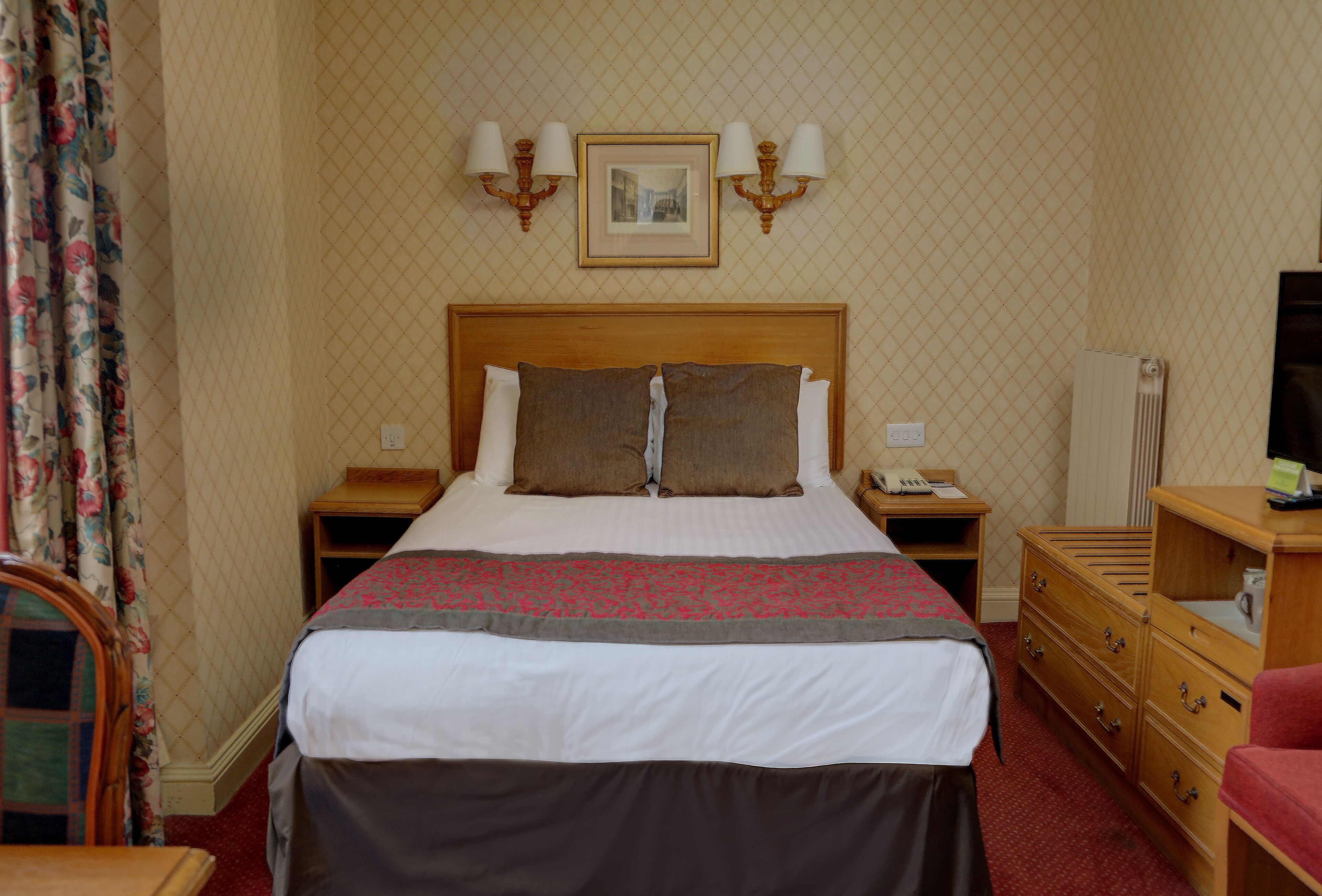 Une chambre d’hôtel avec un grand lit, une tête de lit en bois, deux tables de chevet, une commode et un téléviseur.