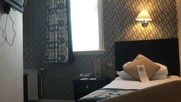 A hotel room with a bed, a bedside table, a lamp, a TV mounted on the wall, and a window with curtains.