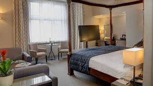 A four-poster bed with a TV, a desk with a lamp, and a seating area with chairs.