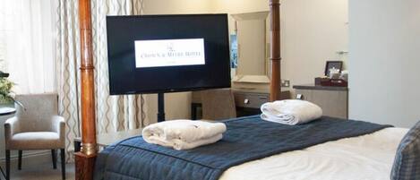 Una cama con dosel, un televisor sobre un mueble bajo, una silla y un escritorio en una habitación de hotel.