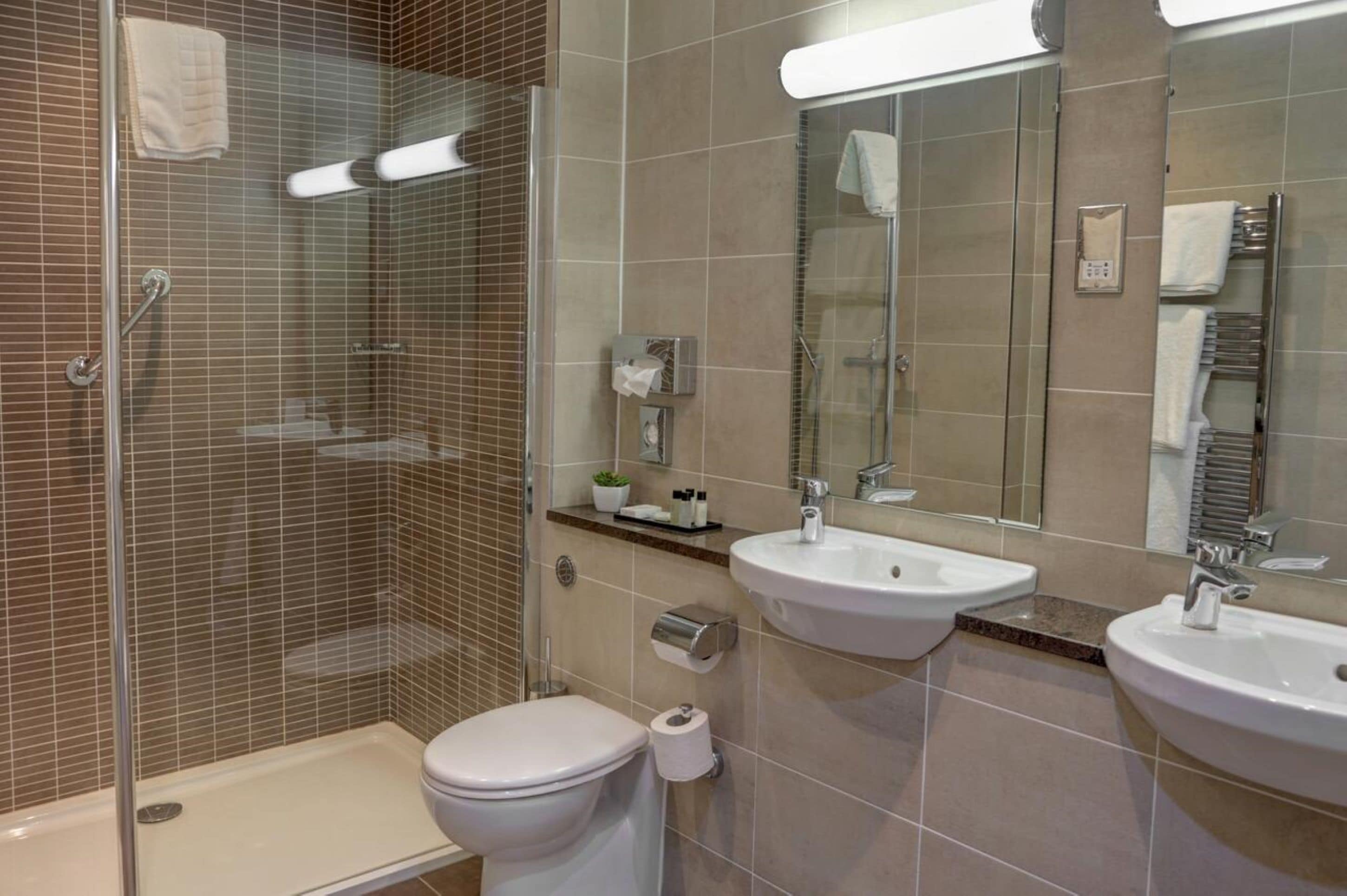 A modern bathroom with a glass-enclosed shower, two sinks, a toilet, and a mirror.