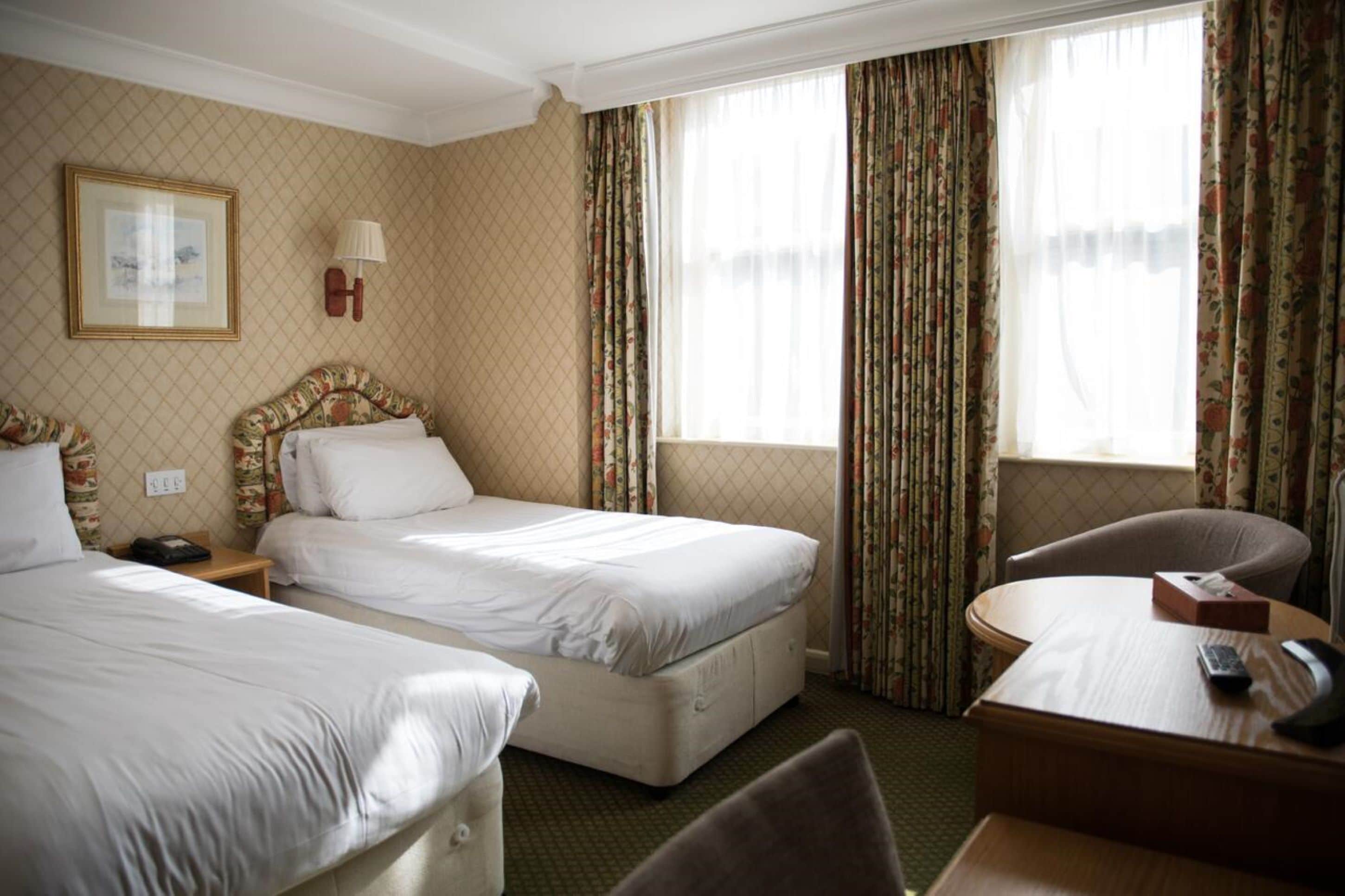 A hotel room with two beds, a desk, a chair, a lamp, and a framed picture on the wall.