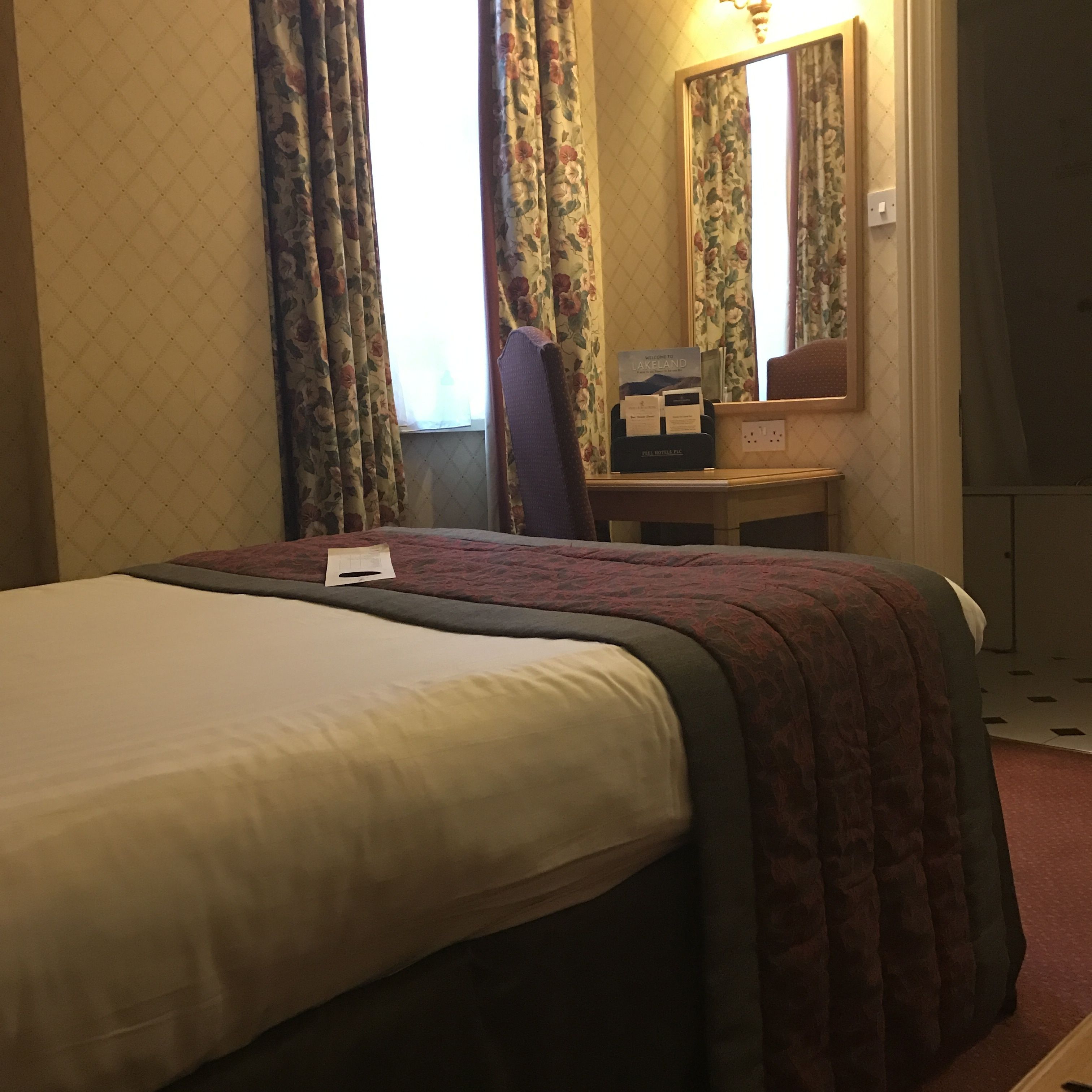 A hotel room with a bed, a desk, and a mirror.