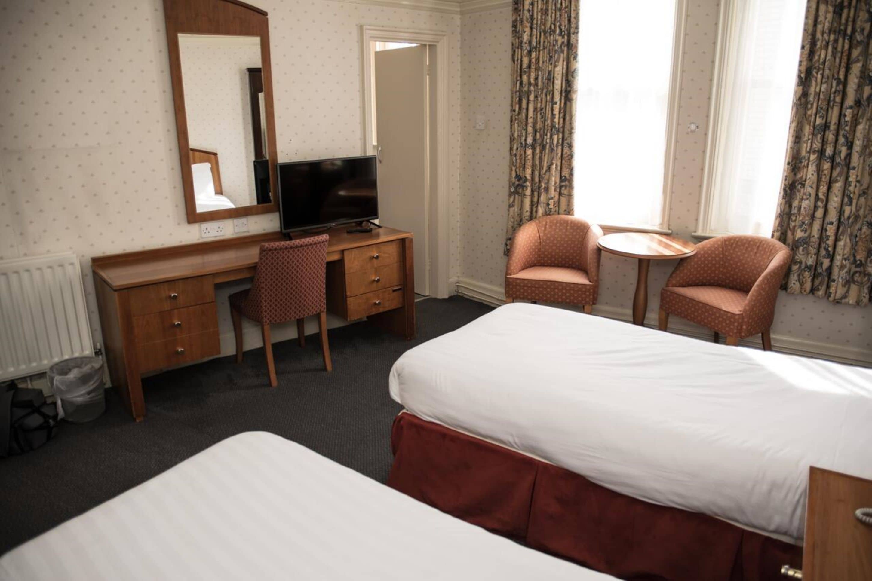 Ett hotellrum med en säng, ett skrivbord med en tv, två fåtöljer och ett litet bord.