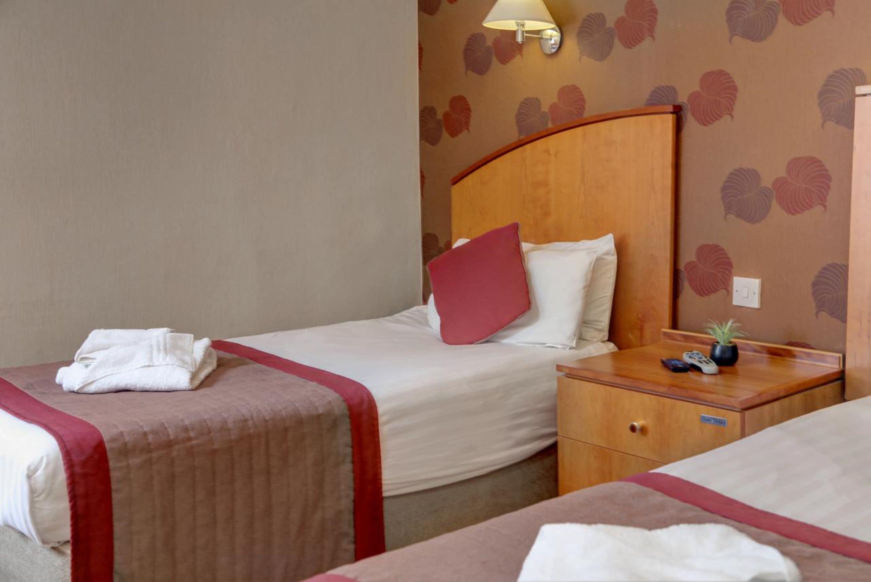 Een hotelkamer met twee bedden, een nachtkastje, een lamp en een muur met een bladmotief.