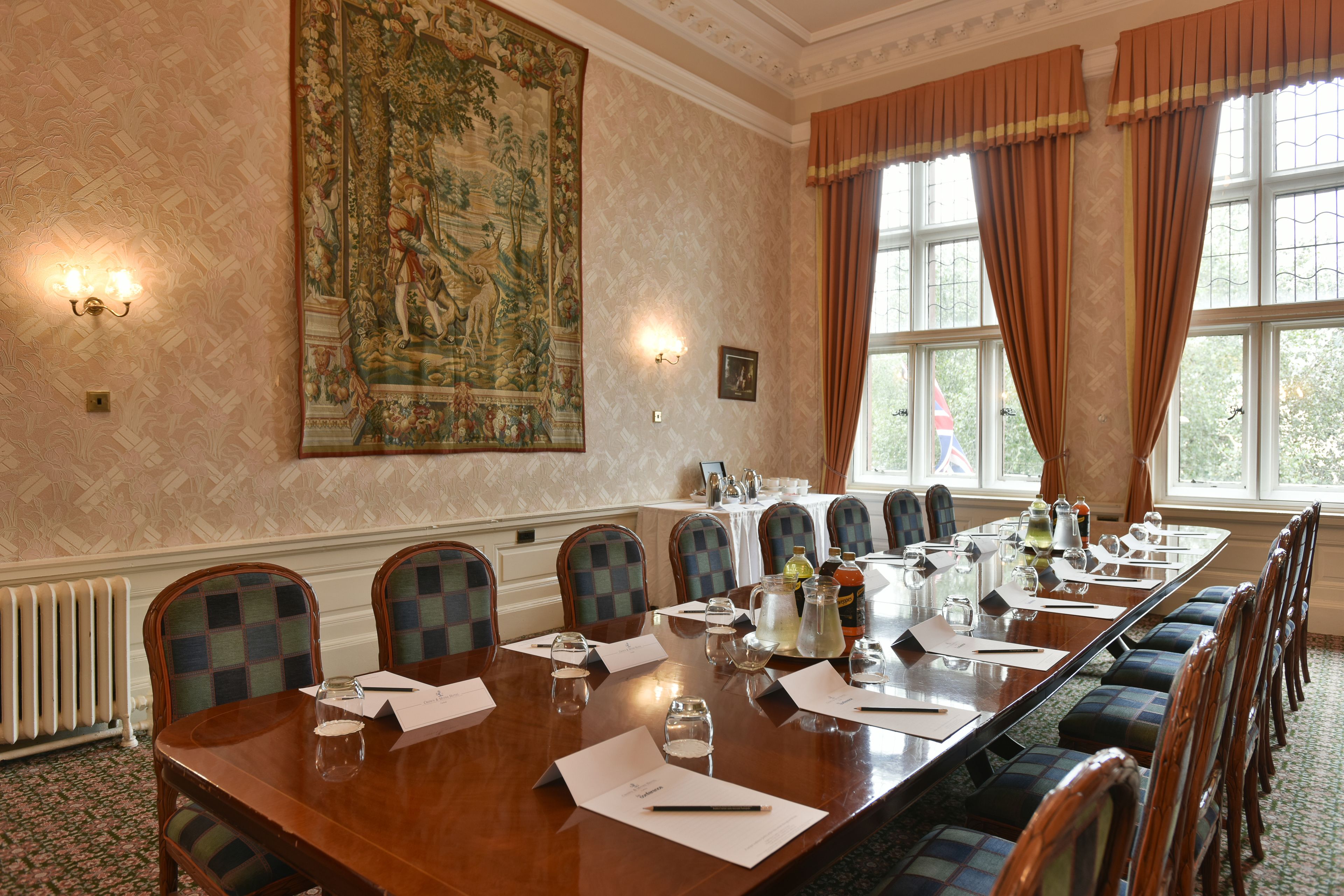 A conference room with a long table, chairs, and a large tapestry on the wall.
