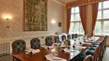 A conference room with a long table, chairs, and a large tapestry on the wall.