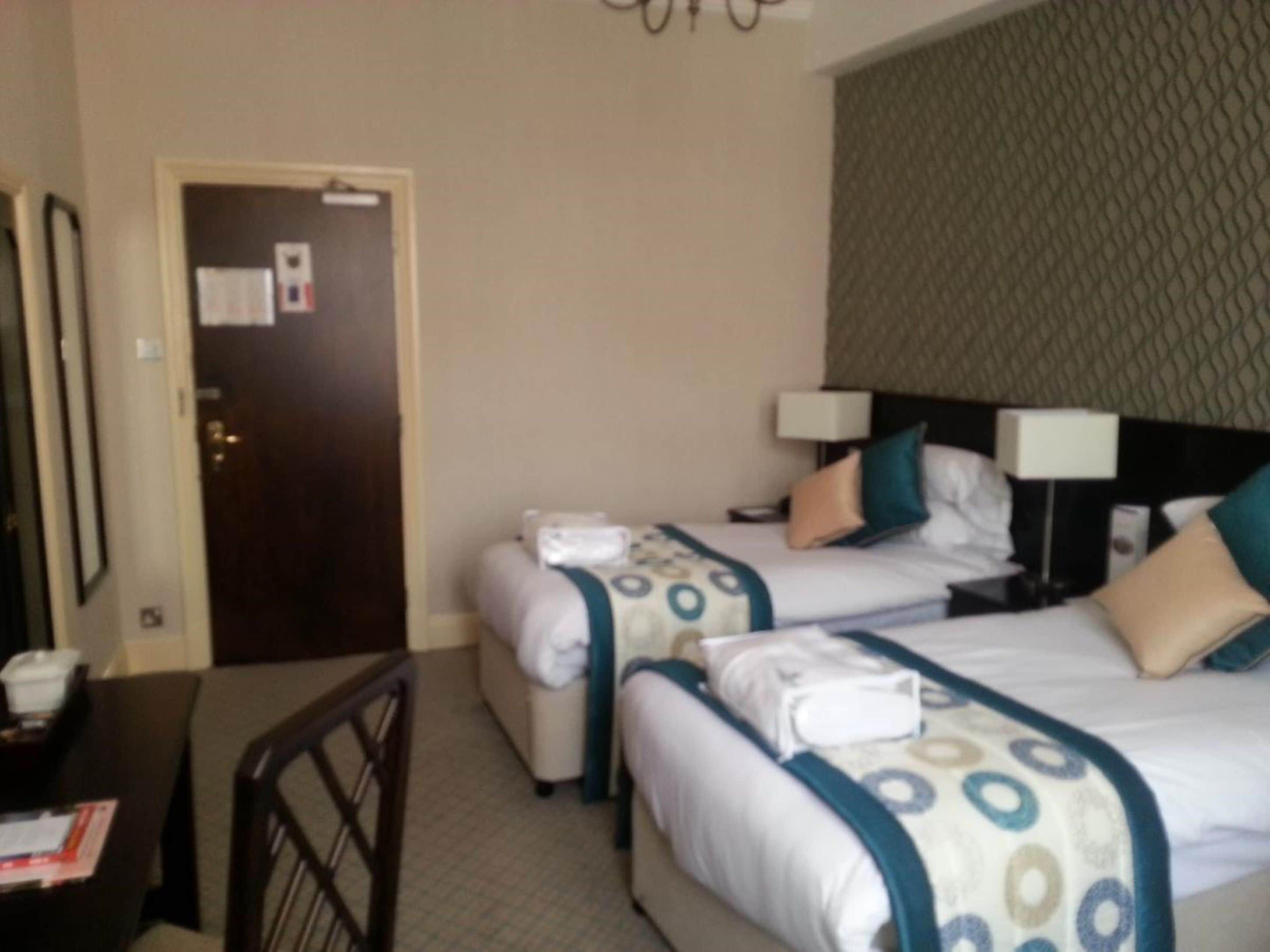 A hotel room with two beds, a desk, and a chair. There is a door with a notice on it.