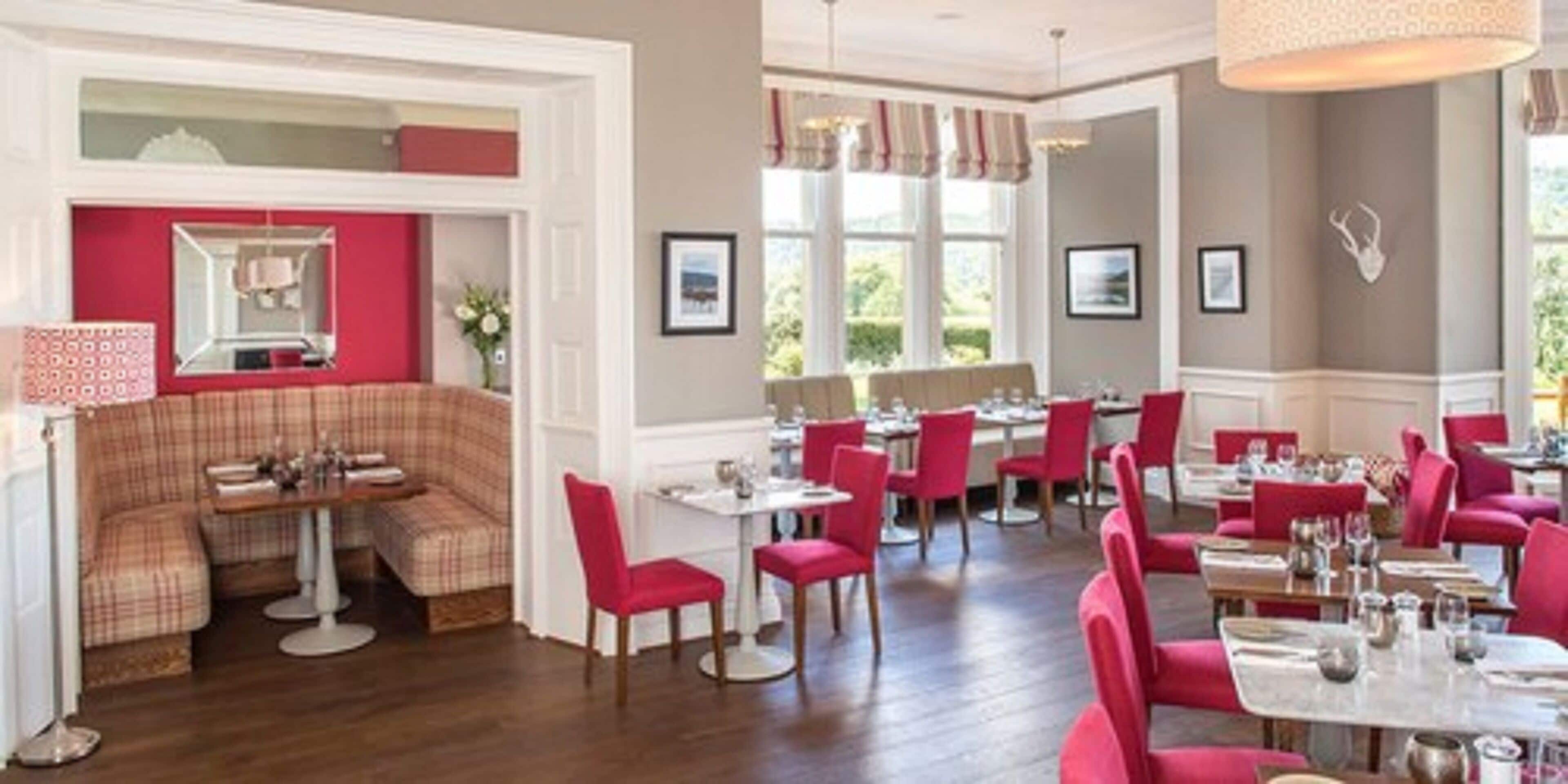A dining area with red upholstered chairs and tables, a red accent wall, and a white ceiling.