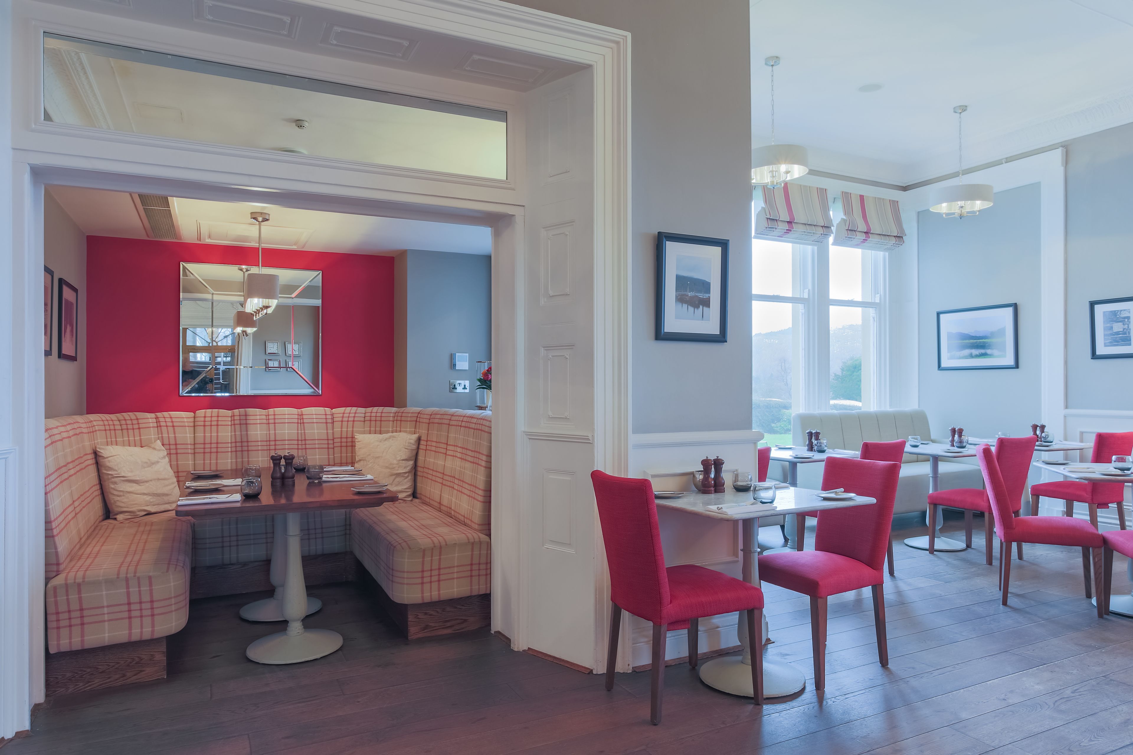 A dining area with a red and beige checkered sofa, white tables, and red chairs.