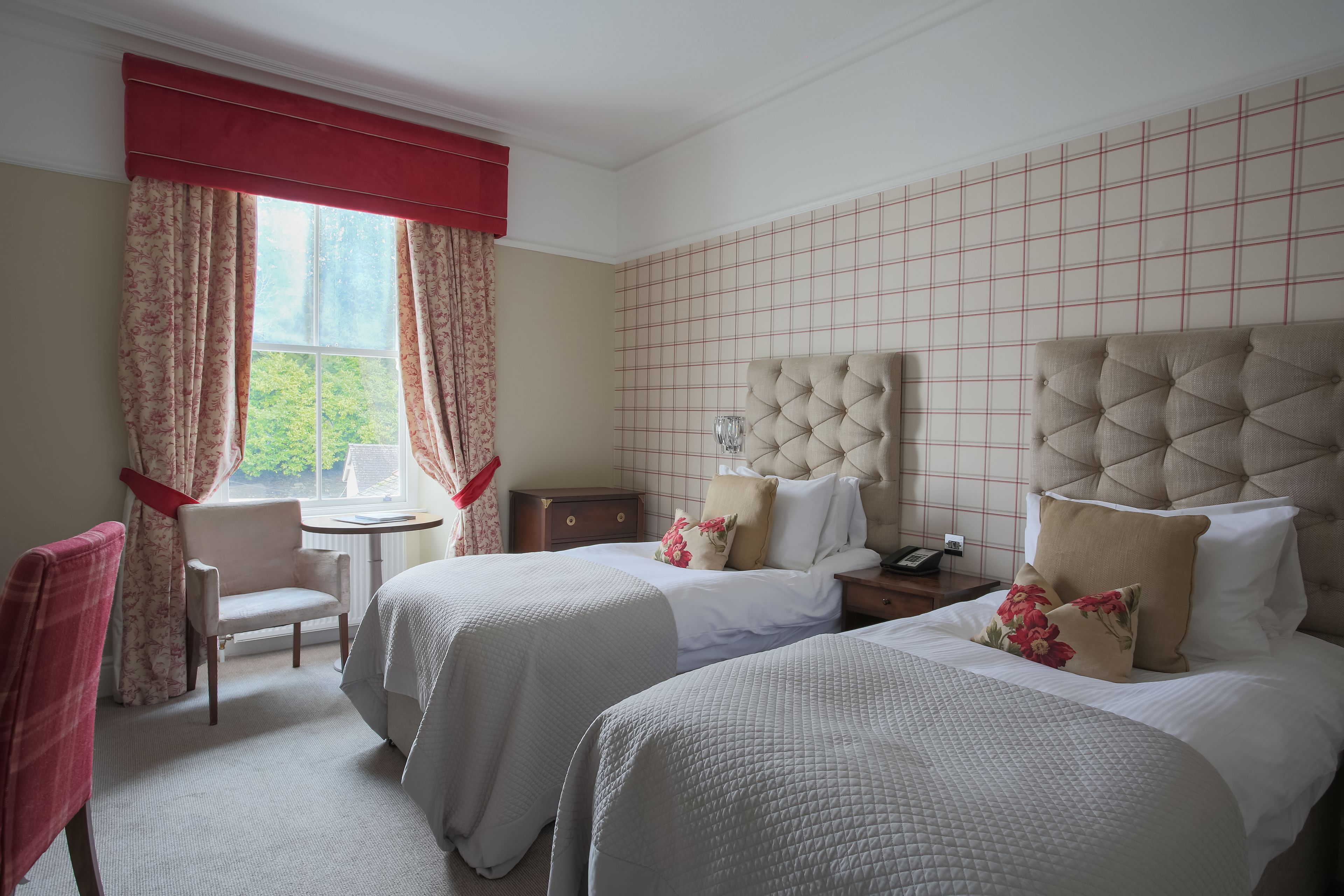 Habitación de hotel con dos camas, una silla, una mesita y una ventana con cortinas.