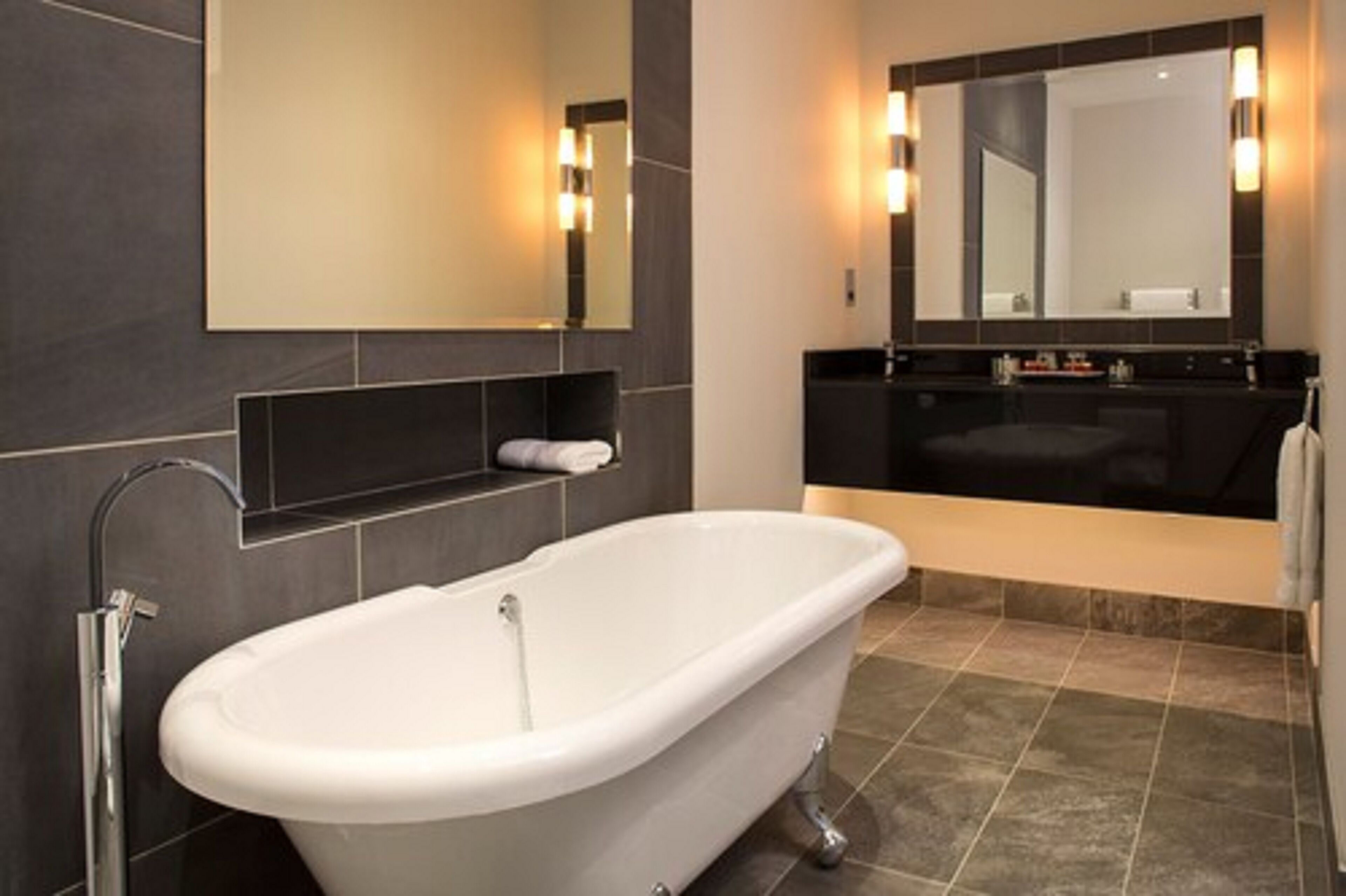 Une salle de bain moderne avec une baignoire sur pieds, un grand miroir et un meuble-lavabo aux tons foncés.
