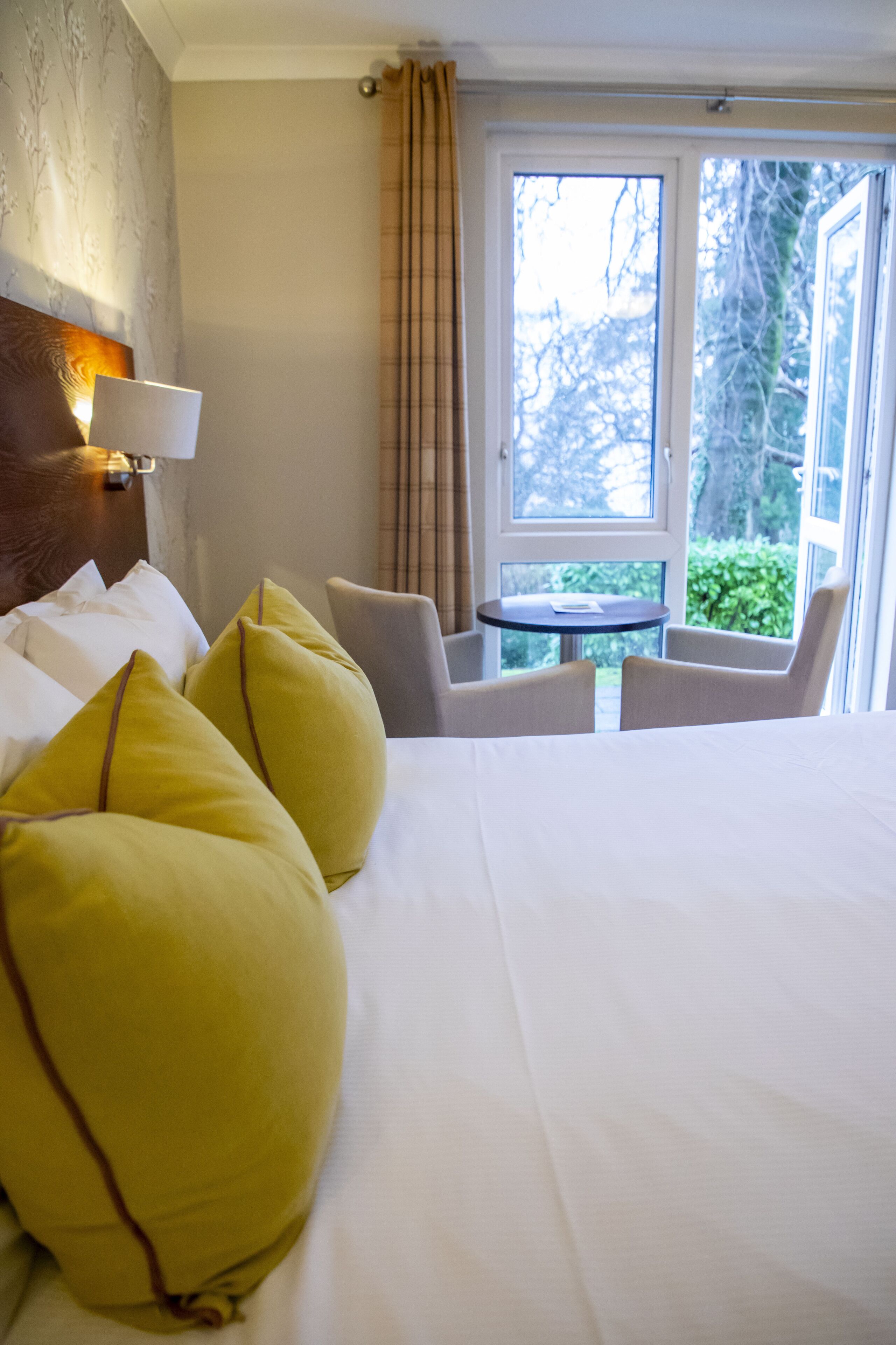 A hotel room with a large bed, yellow pillows, a round table, and chairs.