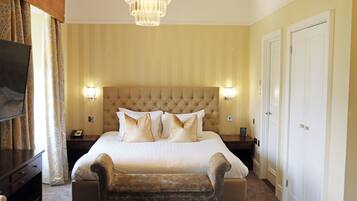 A hotel room with a large bed, two bedside lamps, a television, and a chandelier.