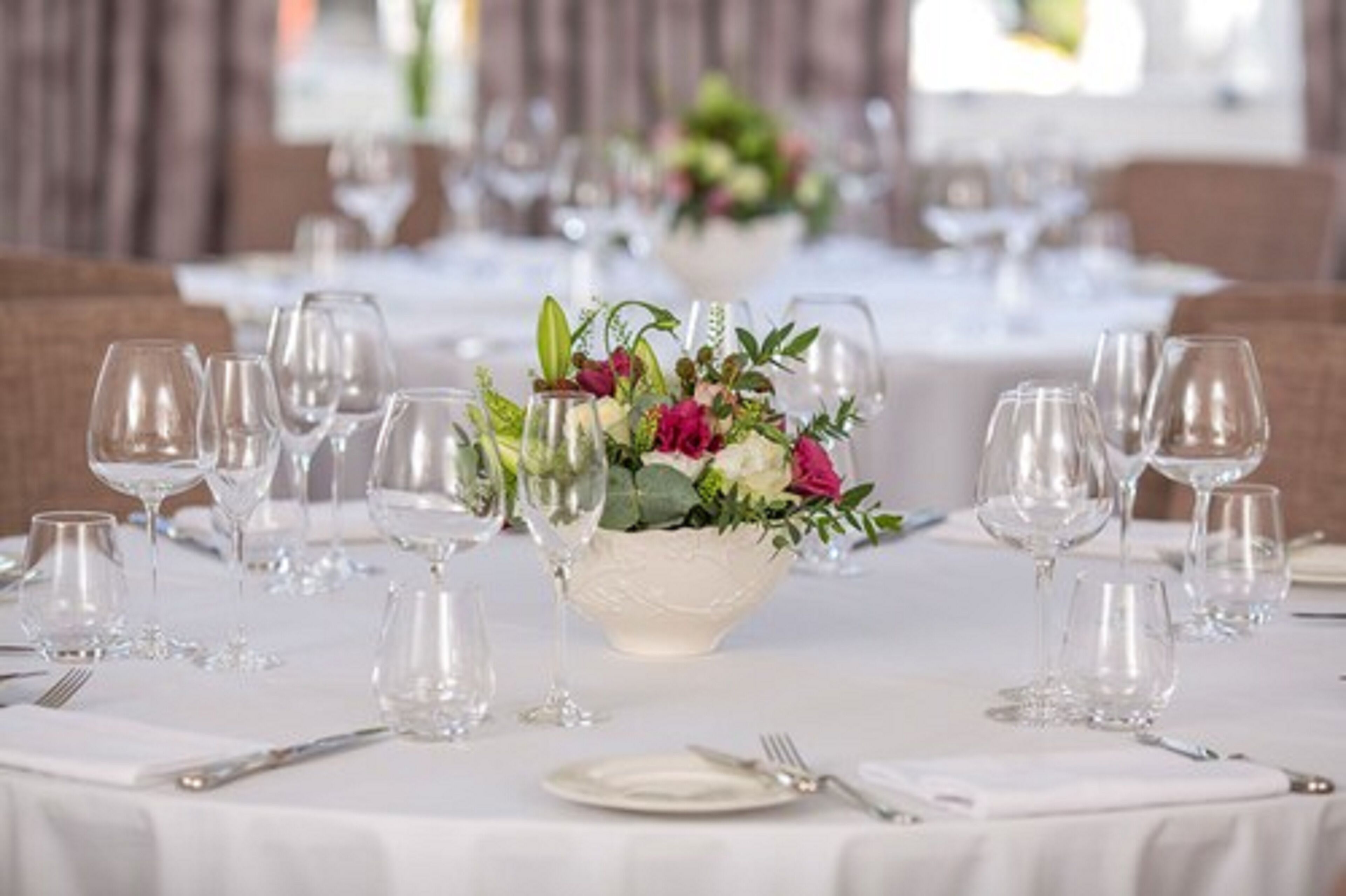 Mesa de comedor dispuesta con varias copas de vino y un centro de mesa con flores.