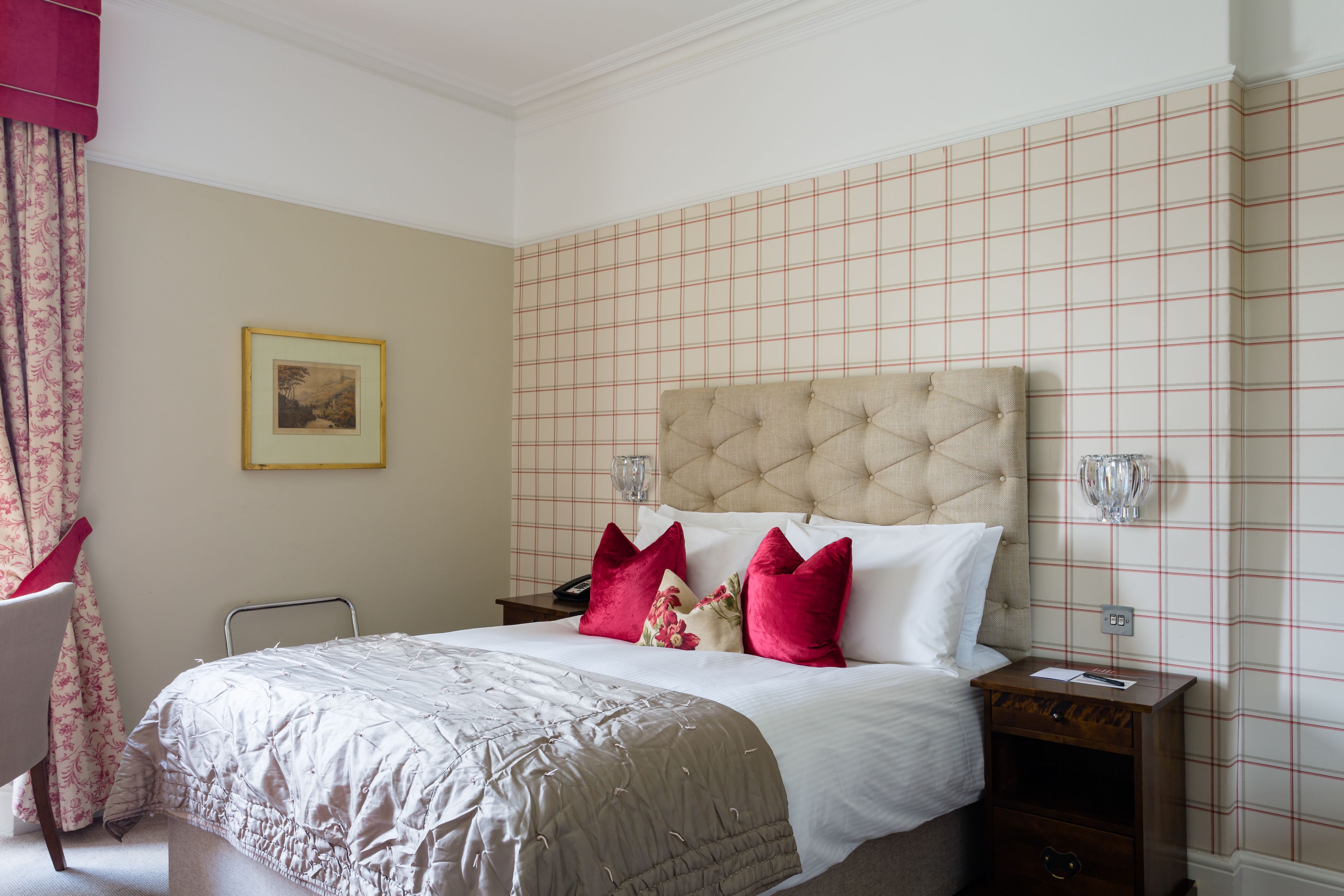 A neatly made bed with a tufted headboard, a bedside table with a lamp, and a framed picture on the wall.