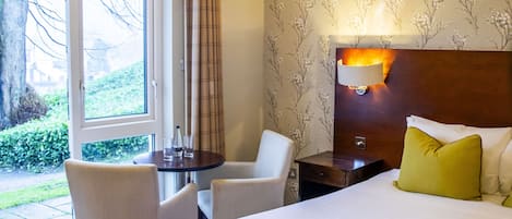 Een hotelkamer met een groot bed, een bureau met twee stoelen, een nachtkastje en een raam met gordijnen.