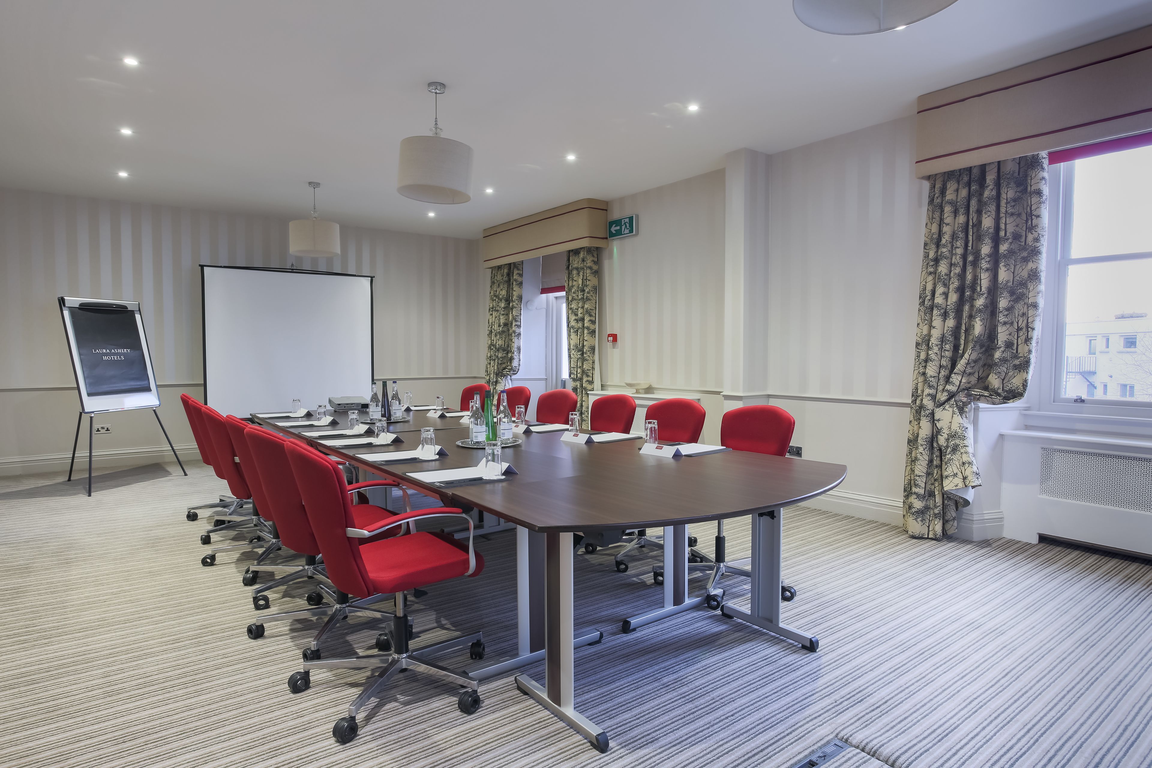 A conference room with a long table, red chairs, a whiteboard, and a projector screen.