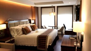 Una habitación de hotel con una cama grande, mesitas de noche, un escritorio, una silla y un televisor.