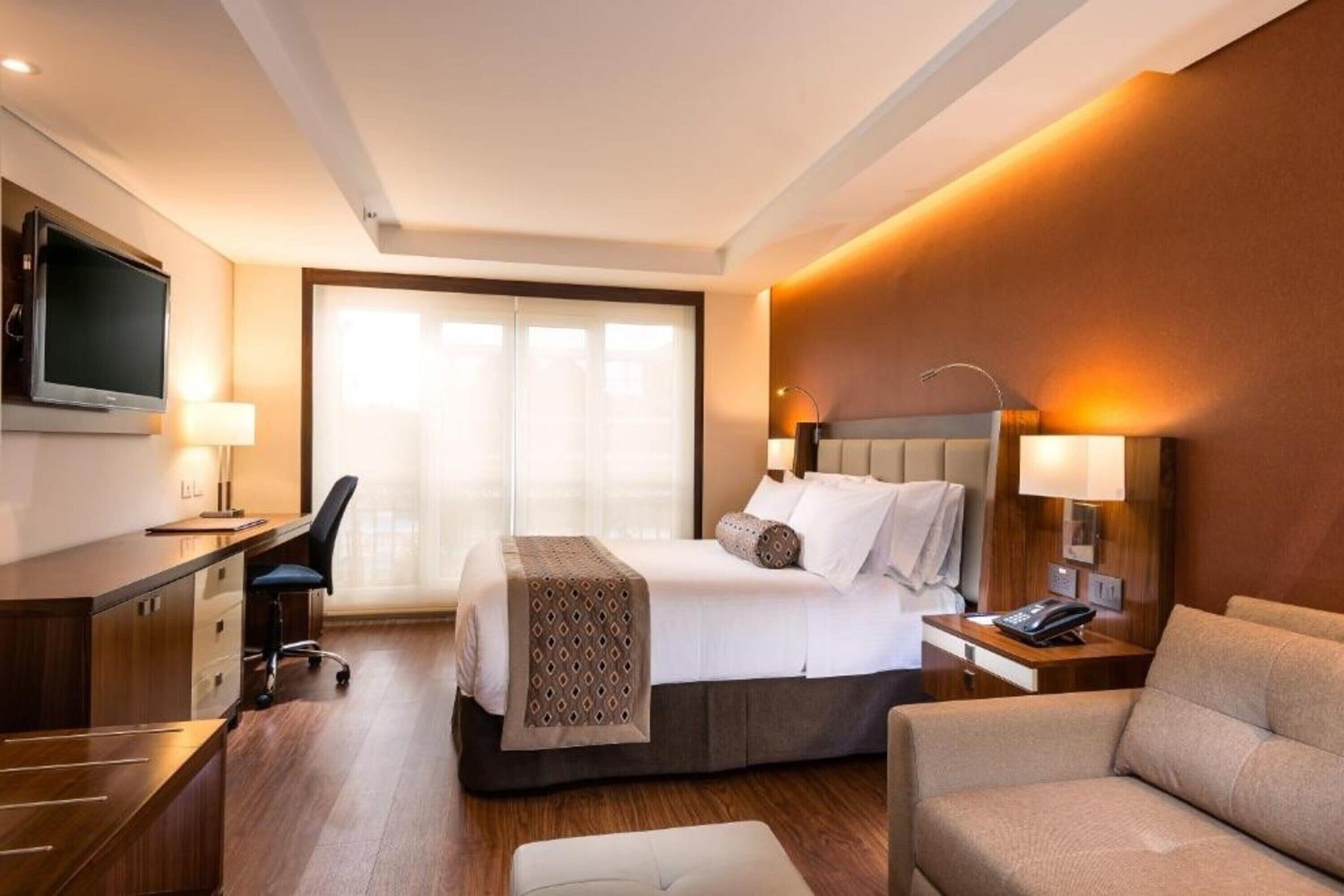 A hotel room with a bed, desk, chair, and a television.