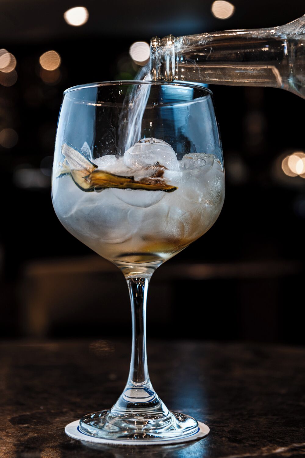 Un bicchiere con cubetti di ghiaccio che viene riempito con un liquido trasparente, forse acqua o un distillato, in un bar.