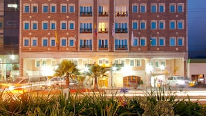 Un hotel a più piani con una facciata simmetrica, caratterizzato da un ingresso centrale con tenda e una serie di balconi.