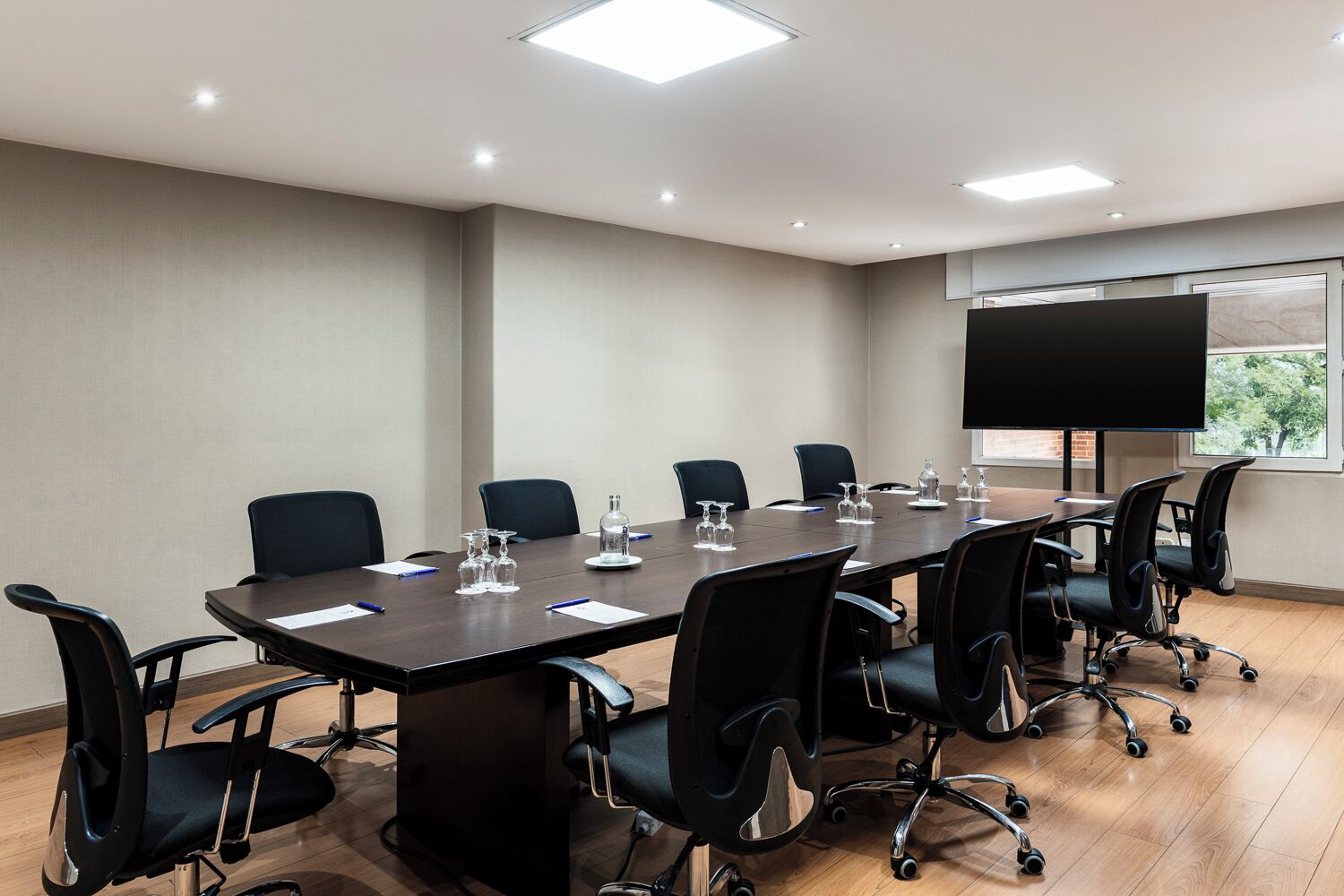 A conference room with a long table, black chairs, and a large screen.