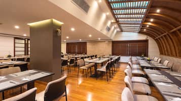 Un salón de conferencias con largas mesas, sillas y un alto techo con tragaluces.