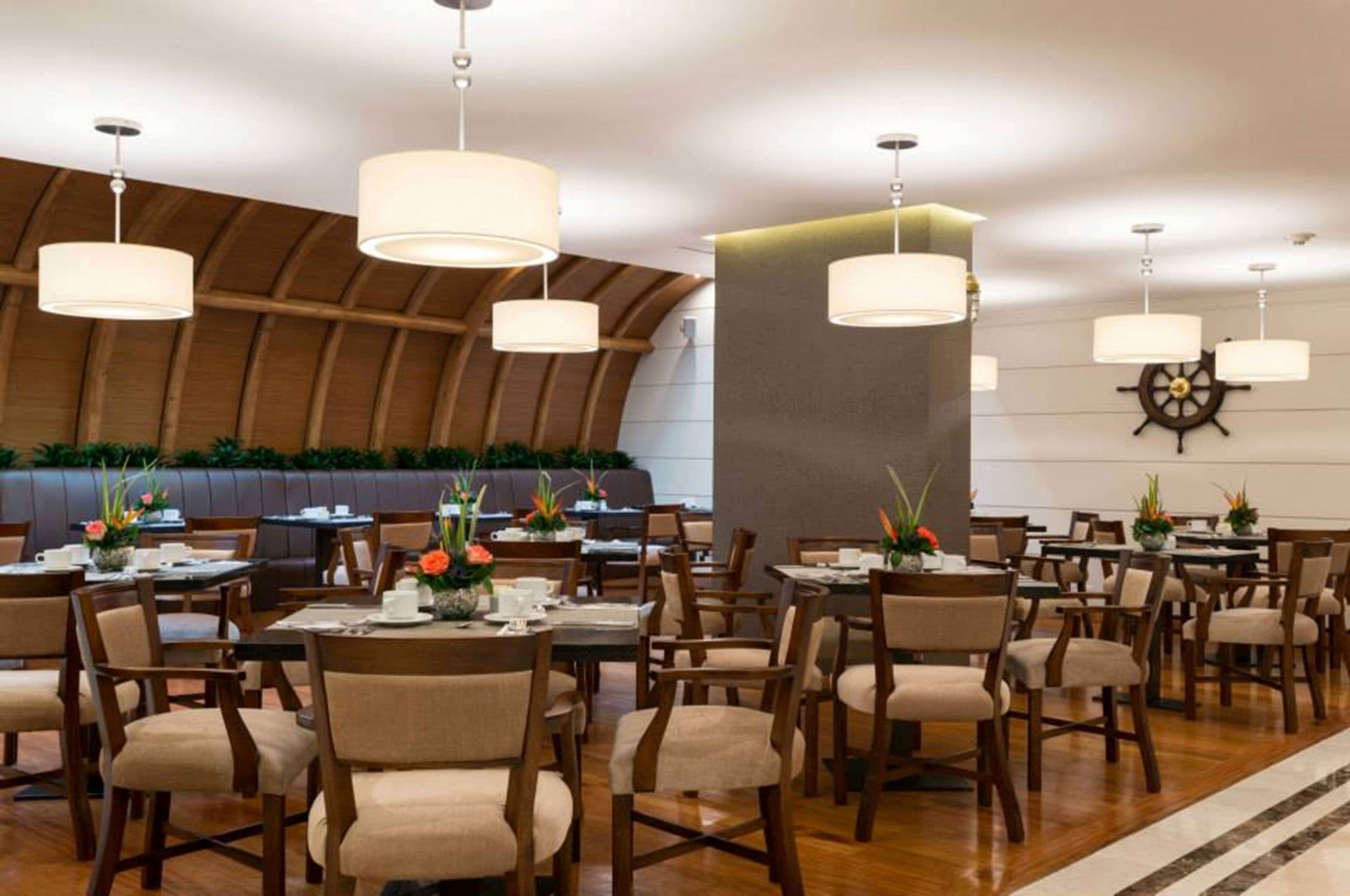 A restaurant with round tables, chairs, and hanging pendant lights.