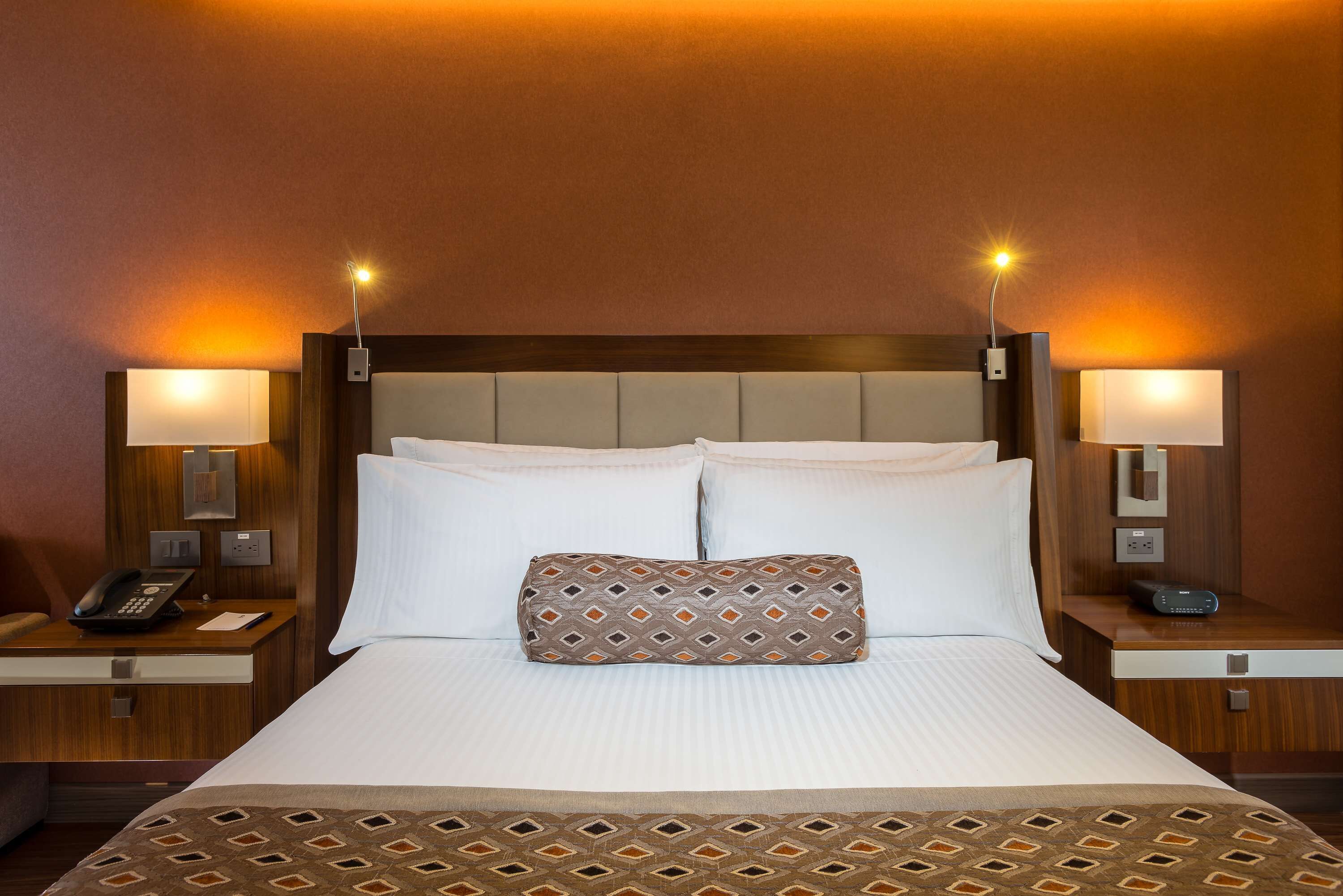 A hotel room with a large bed, two bedside tables, a telephone, and two wall-mounted lamps.