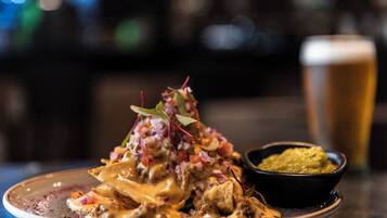 A plate of nachos topped with cheese, onions, and a green sauce, accompanied by a glass of beer and a small bowl of green sauce.