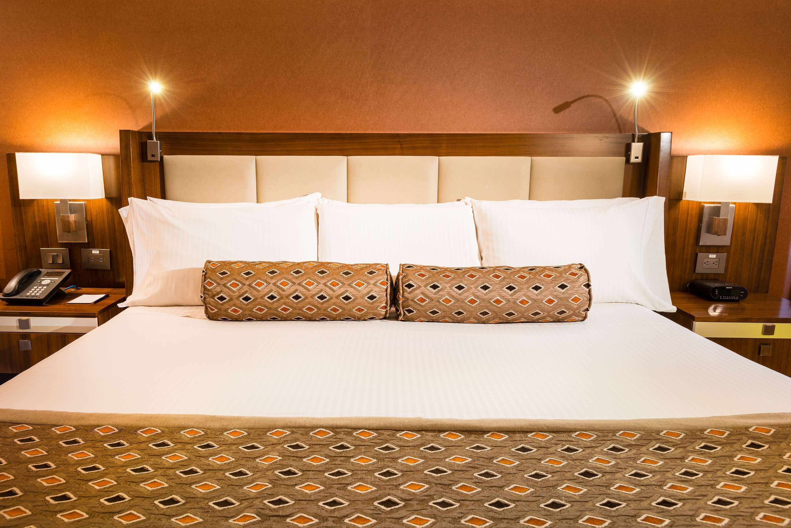 Una habitación de hotel con una cama grande, dos lámparas de noche, un teléfono y una mesita de noche.