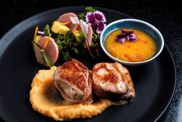 A plate with two pieces of meat, a side of mashed potatoes, and a bowl of soup.