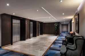 Un hall d’hôtel avec un long couloir, des ascenseurs, un comptoir d’accueil et une moquette à motifs.