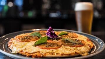 Pizza com fatias de tomate e ervas sobre um prato, acompanhada de um copo de cerveja.
