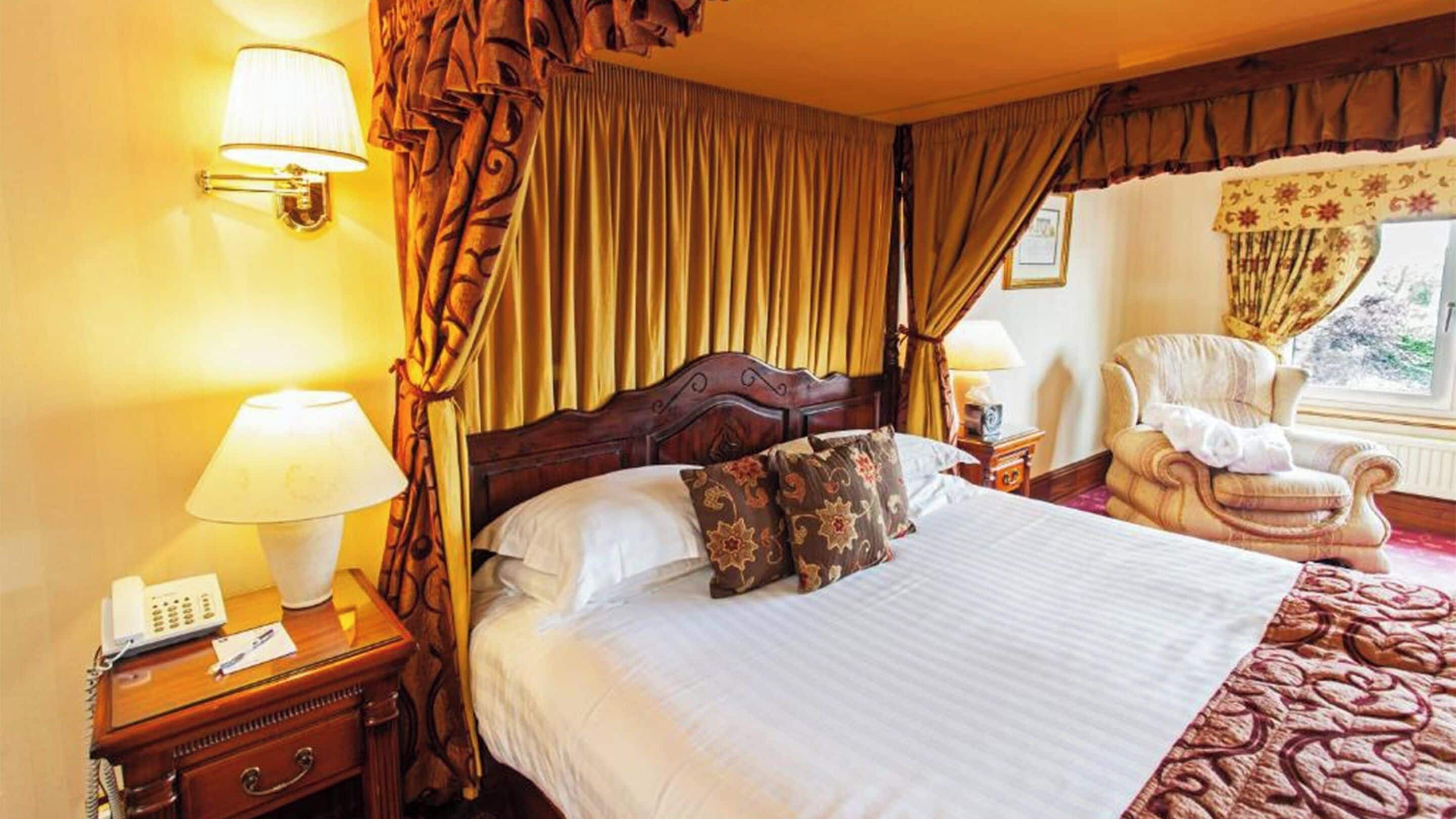 Een hotelkamer met een groot bed, twee bedlampen, een telefoon, een stoel en een raam met gordijnen.