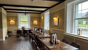 A restaurant with a long wooden table, brown leather chairs, and large windows with a view of greenery.