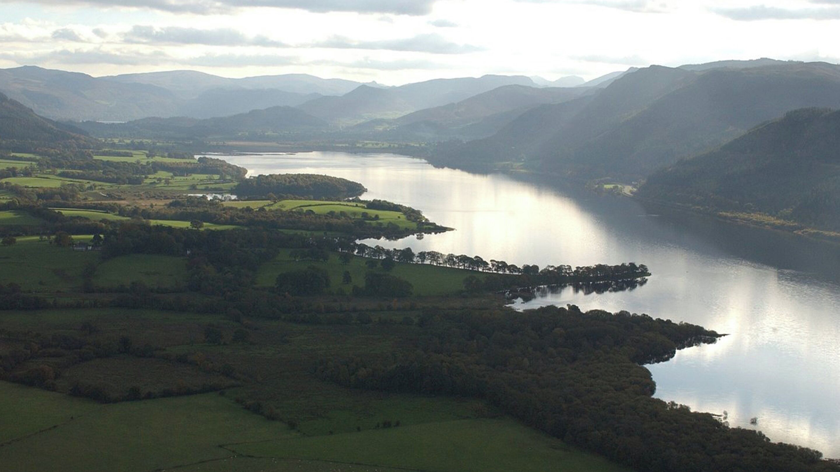 A panoramic view of a lake surrounded by rolling hills and a distant mountain range.