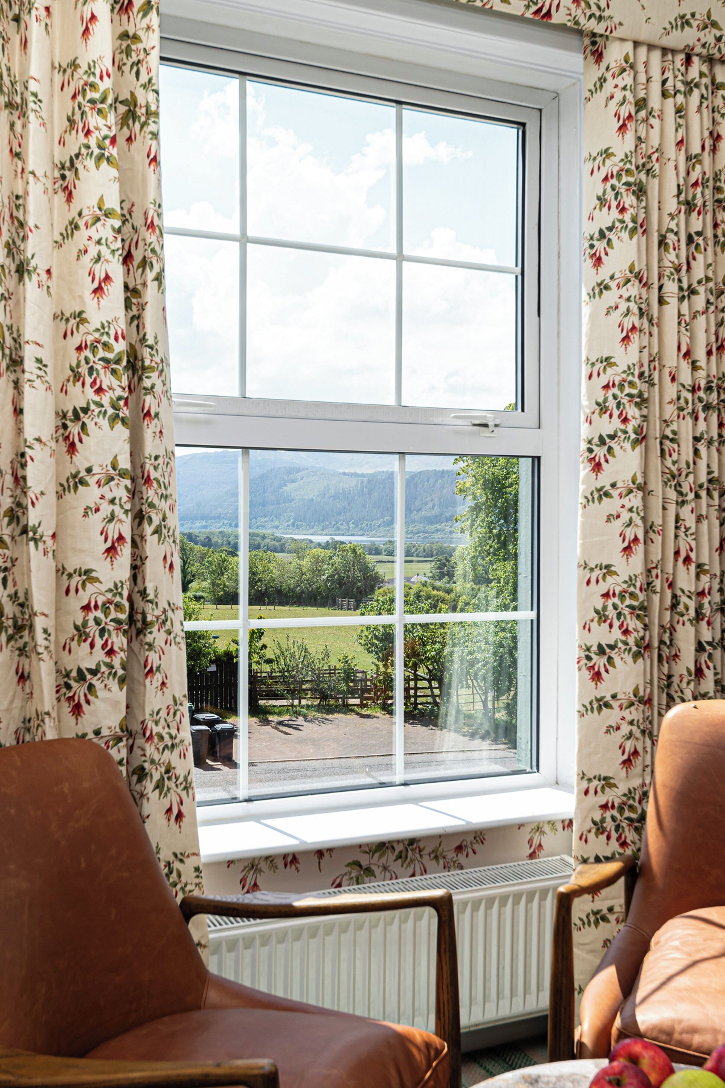 Una habitación con un ventanal grande, cortinas florales y dos sillones de cuero.
