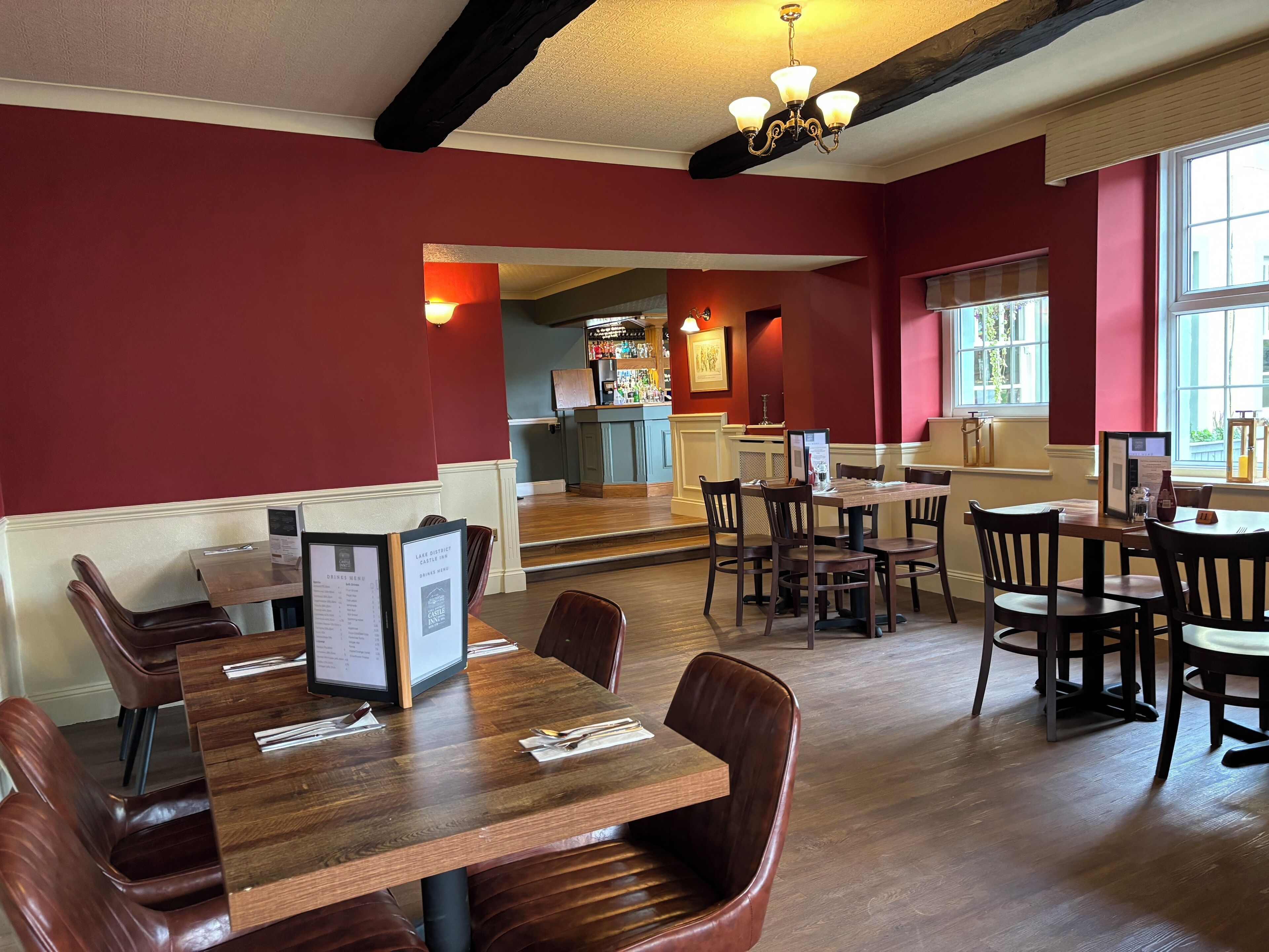 Un restaurant avec des tables en bois et des banquettes en cuir, un bar situé au fond de la salle et de grandes fenêtres laissant entrer la lumière naturelle.